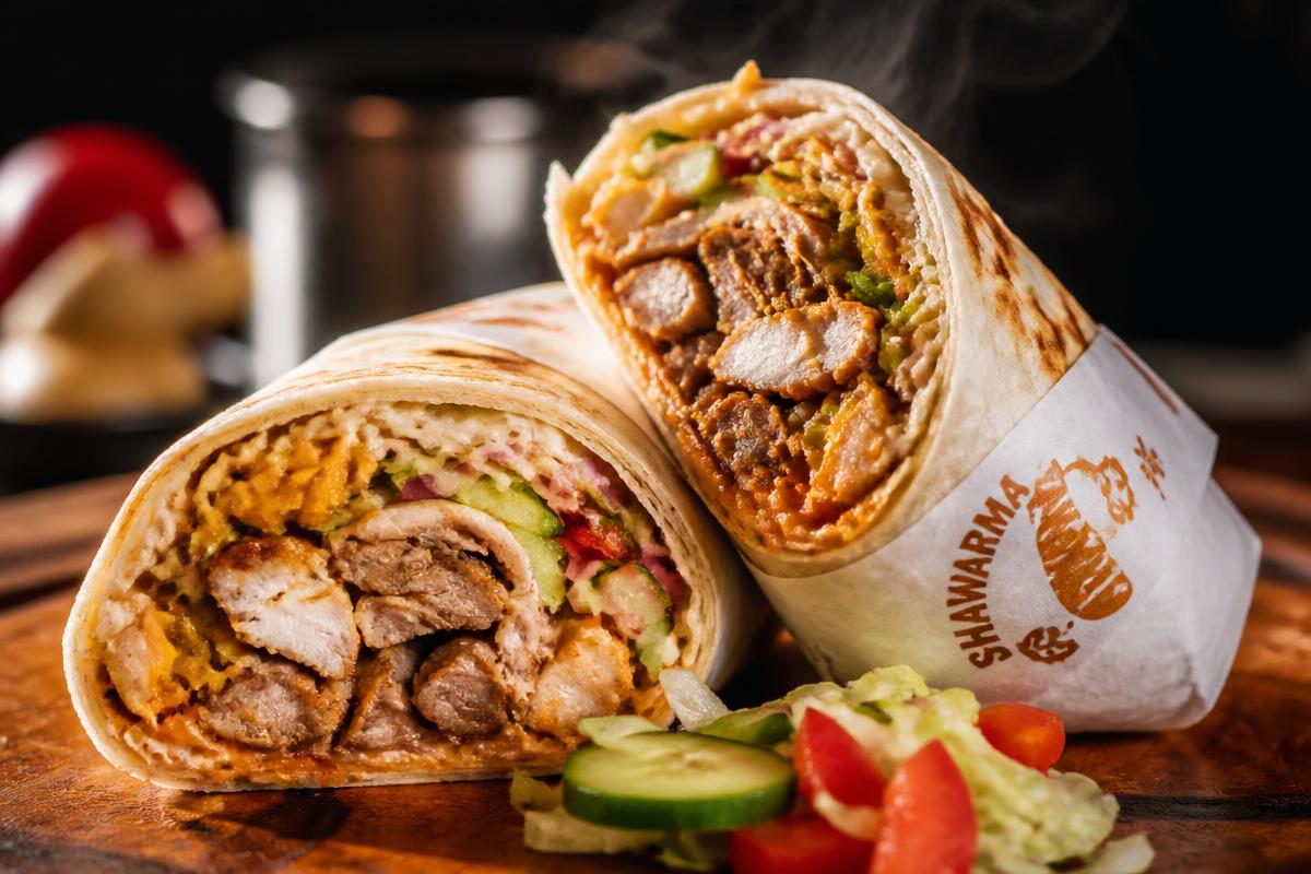 A steaming hot Chizzy Hub shawarma wrap sliced in half with fresh vegetables